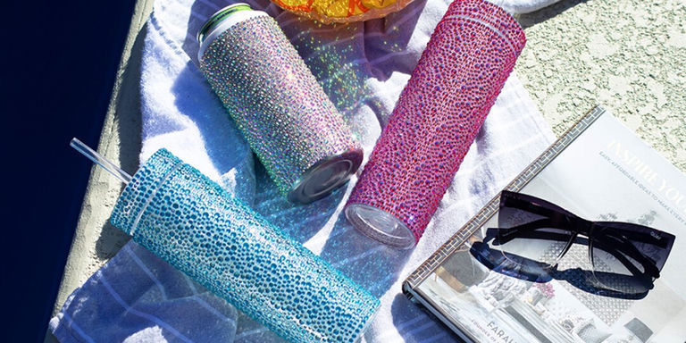 brillantes vasos de cristal con pedrería y enfriador junto a gafas de sol y toalla junto a la piscina