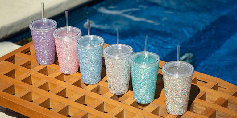Colorful rhinestone glam tumblers with straws lined up on pool deck
