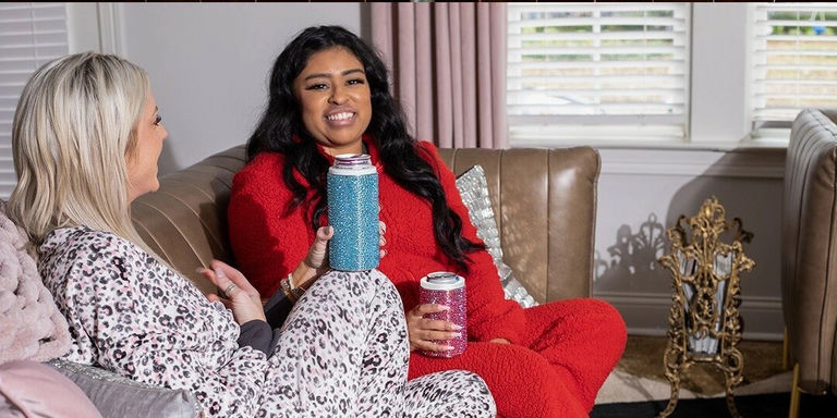 two women in cozy loungewear holding rhinestone drinkware on couch