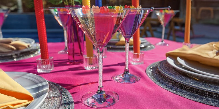 colorful Pride cocktails served in rhinestone martini glasses with rainbow gummy garnish on hot pink tablecloth