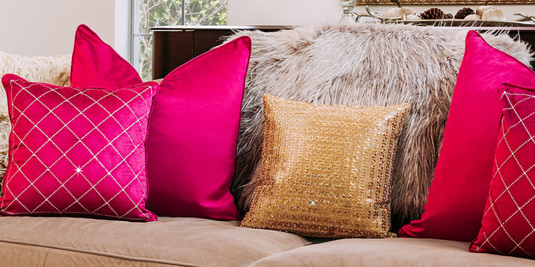Almohada de cuentas doradas superpuesta con almohadas de terciopelo rojo y estampadas en un sofá neutral